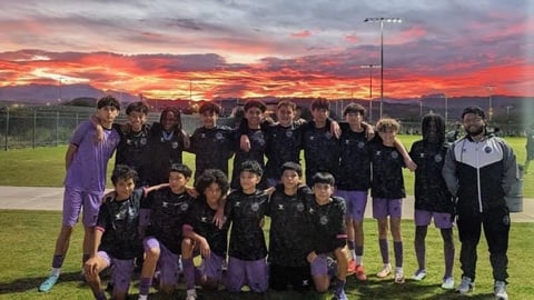 Youth soccer team posing together on field at sunset with dramatic orange and pink sky in background