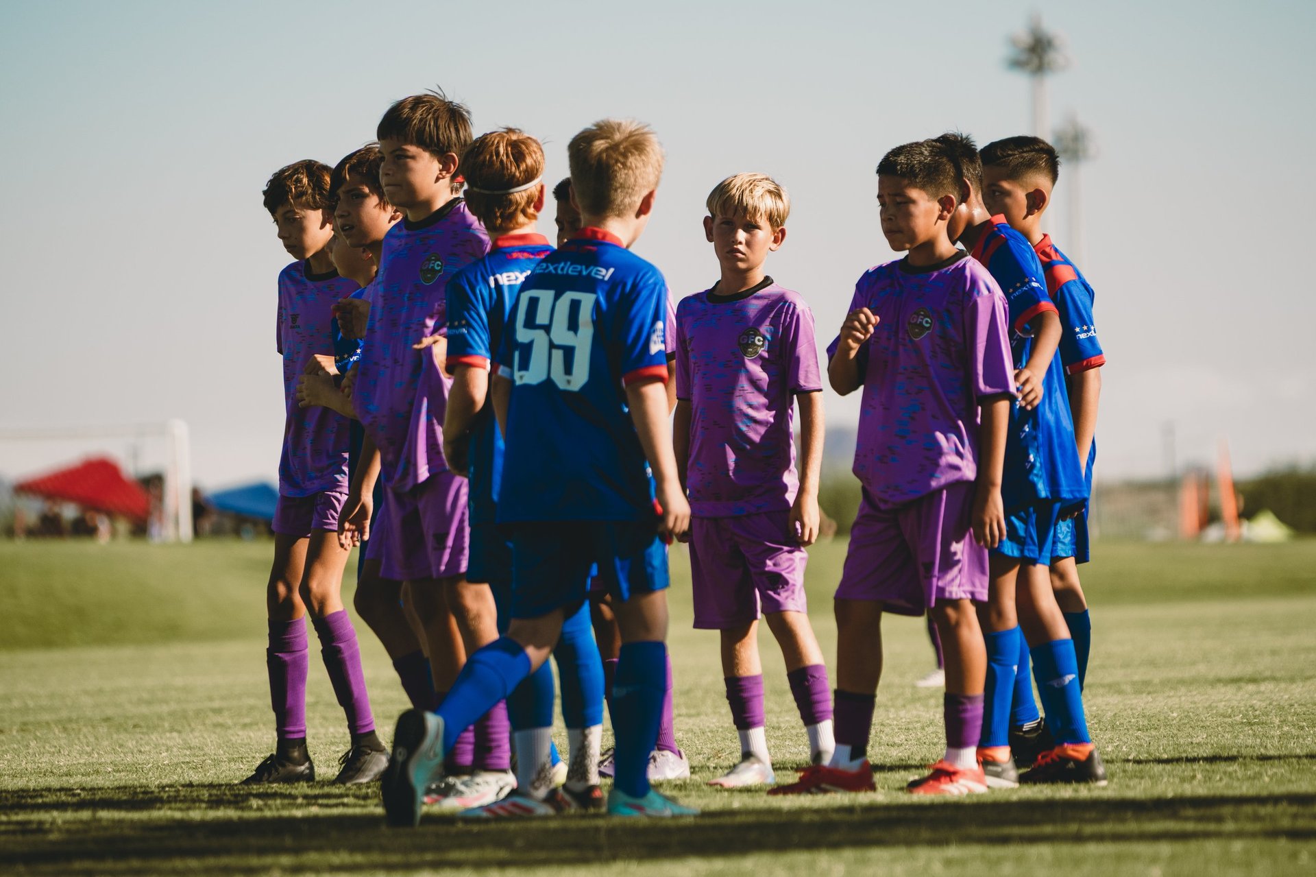 Group of young soccer players in purple and blue uniforms huddle together on a grass field