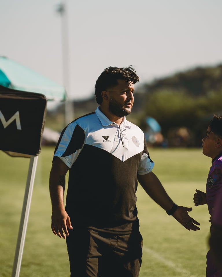 Man in blue and black sports jersey standing on a grass field during daytime, conversing with another person
