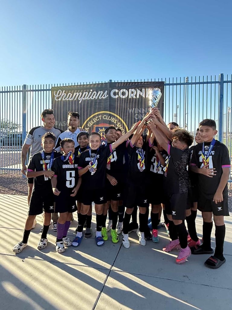 Youth soccer team in black uniforms holding a trophy together under a Champions Corner sign