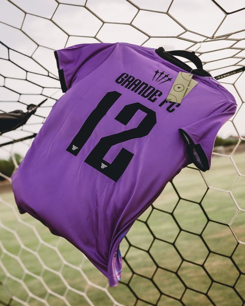 Purple soccer jersey number 12 hanging on goal net with goalkeeper glove visible