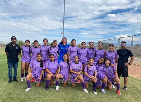 Youth girls soccer team in purple uniforms posing together on field with coaches on sunny day