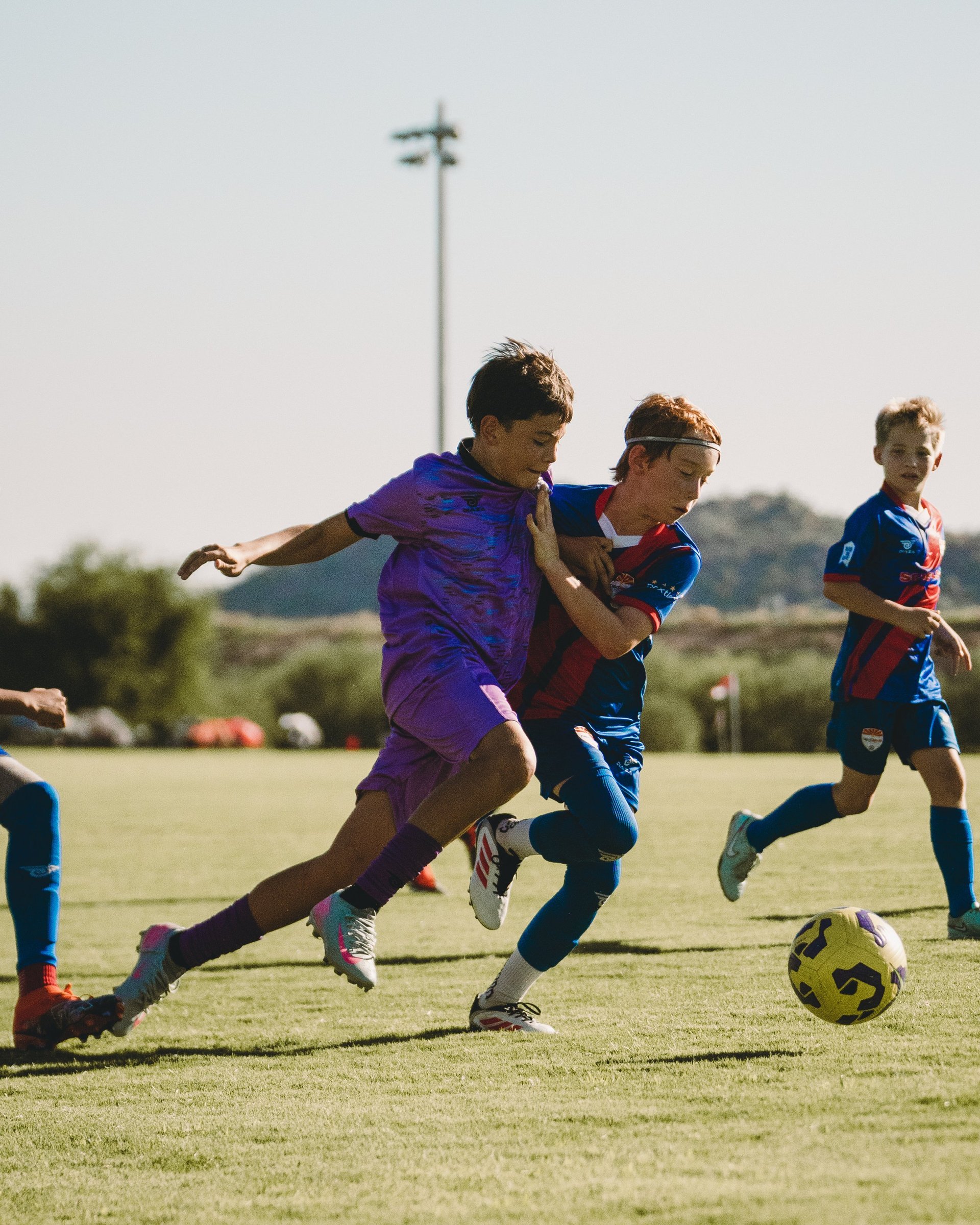 Young soccer players competing for the ball during a youth match on a grass field, with one player in purple and others in blue uniforms