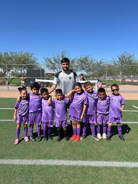 Soccer coach with youth team in purple uniforms posing on grass field at sports complex
