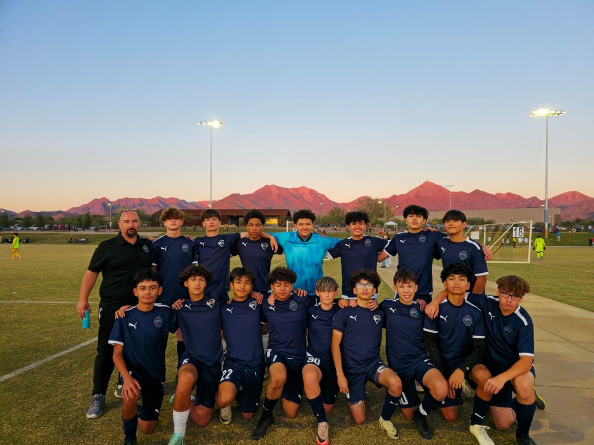 Youth soccer team in blue and black jerseys posing together on a grass field at sunset with mountains in the background