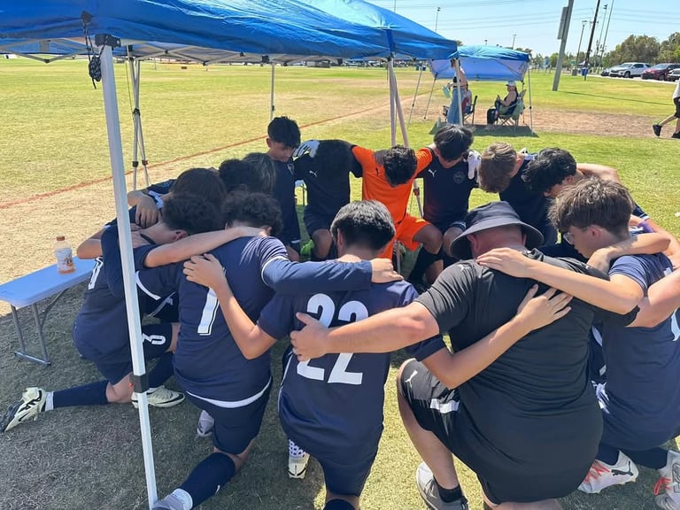Youth soccer team huddled together under blue canopy tent on grass field during game or practice