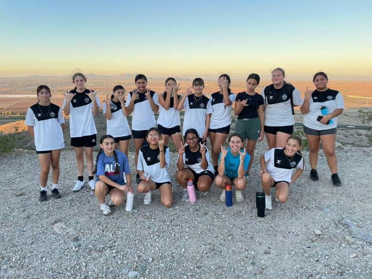 Youth soccer team in black and white uniforms posing together on a hilltop at sunset with desert landscape in background
