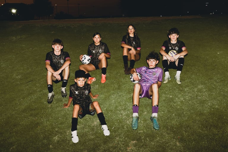 Youth soccer team posing together on grass field at night, wearing black and purple uniforms with soccer balls