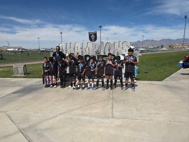 Youth soccer team in black uniforms posing together in front of a Champions sign at a sports complex
