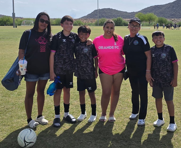 Group of six people standing together on a soccer field with a soccer ball in the foreground and mountains in the background