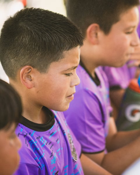 Young boy in purple sports shirt looking to the side, with another child visible beside him