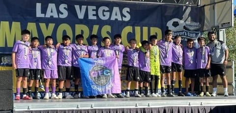 Youth soccer team in purple uniforms on stage at Las Vegas Mayors Cup tournament, holding banner