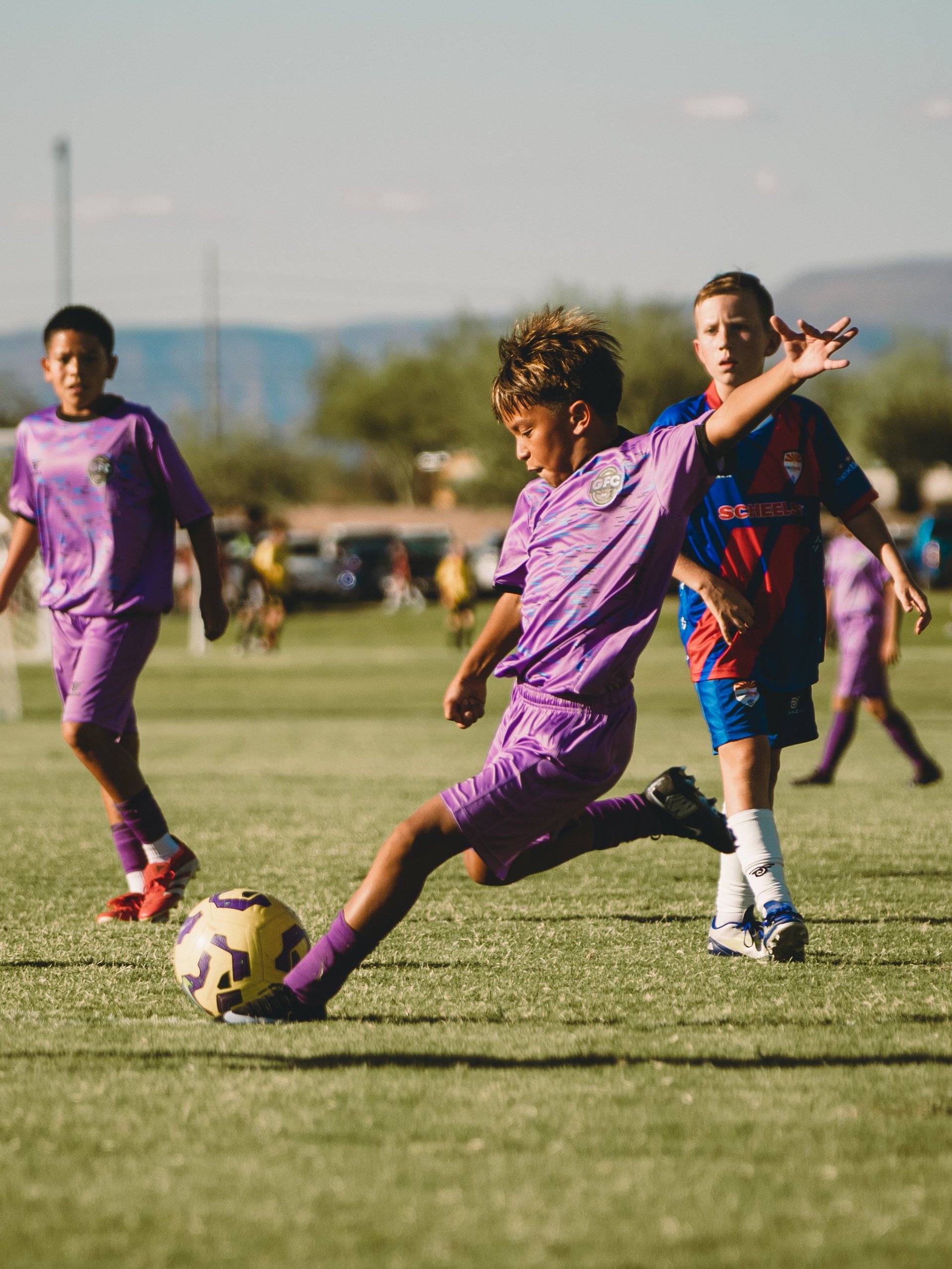 Young soccer player in purple jersey kicking ball during youth soccer match on grass field