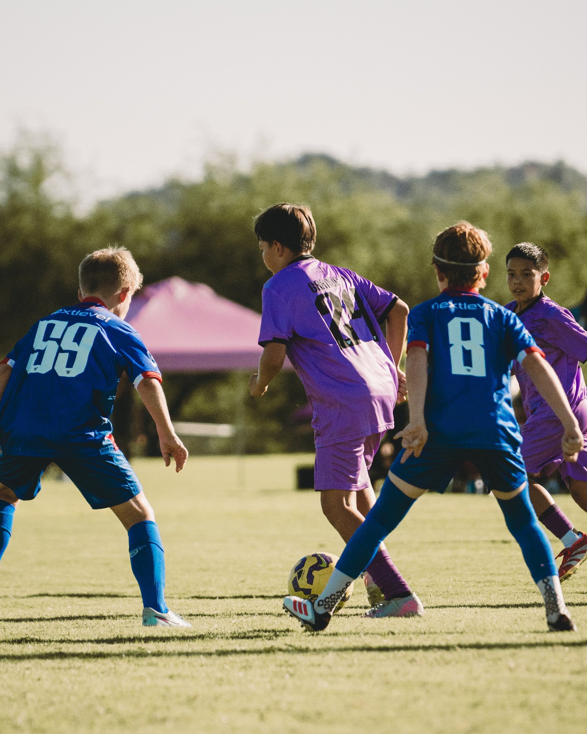 Young soccer players in blue and purple jerseys competing for the ball during a youth match outdoors