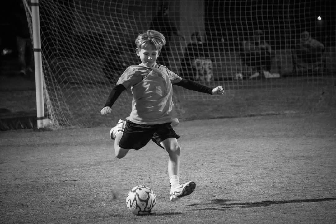 Young soccer player kicking ball on field at night in black and white photo