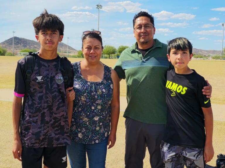 Family of four smiling at an outdoor sports field with mountains in the background