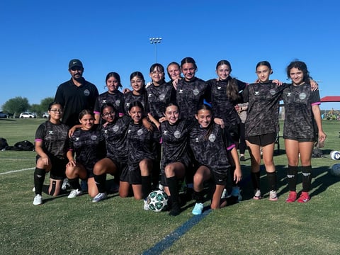Youth girls soccer team in black uniforms posing on field with soccer ball under clear blue sky
