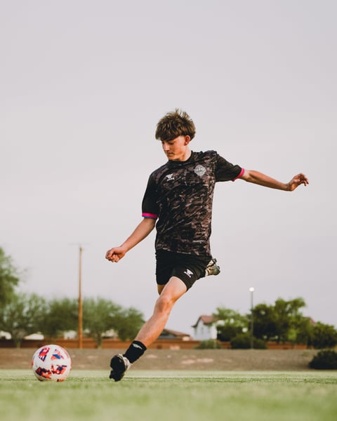 Young soccer player kicking a red and white ball on a grass field during a sunny day