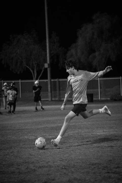 Young soccer player kicking ball during night match, black and white photograph