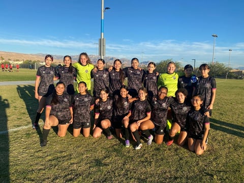 Female soccer team posing together on grass field in matching black uniforms and yellow goalkeeper jerseys